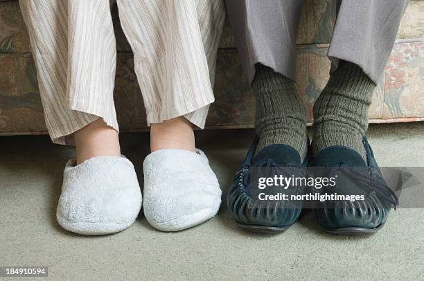 two home slippers worn by people sitting on the couch - old shoes stockfoto's en -beelden