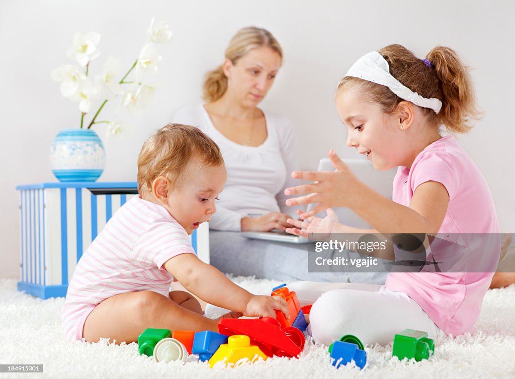 Children playing and mother working on laptop in background