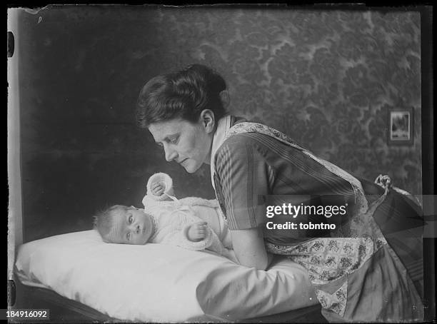 black and white photo of caring mother leaning over her baby - 20s stockfoto's en -beelden