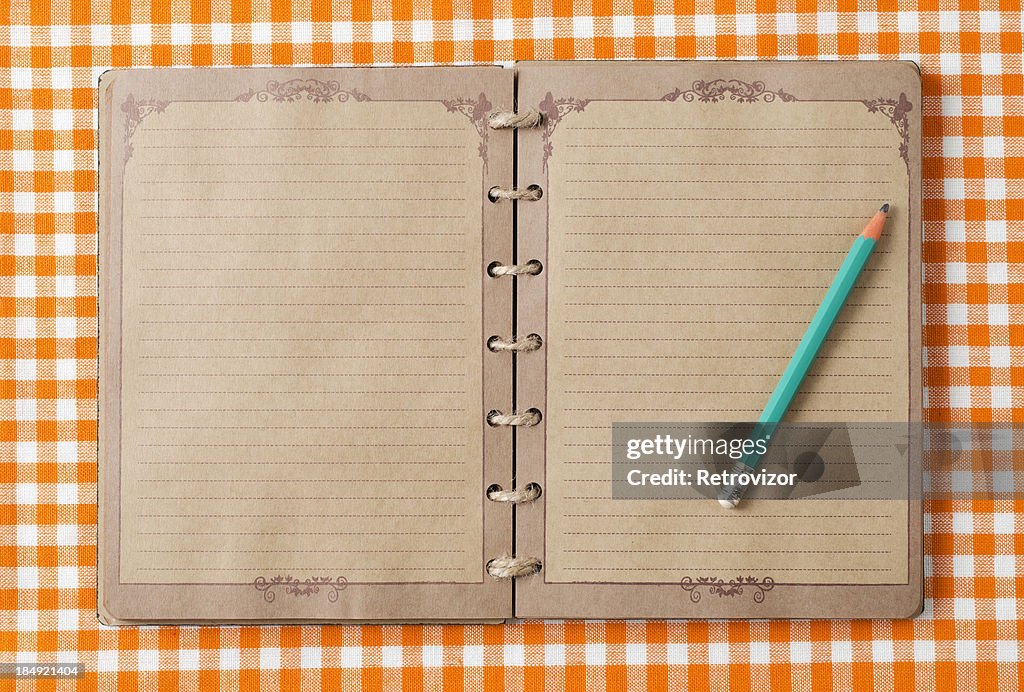 Old notebook and pencil on orange tableclot