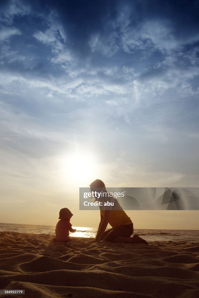Baby and mother figure playing in sand on a beach