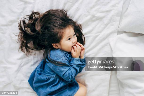 portrait of cute little asian toddler girl laughing joyfully and lying on bed with her panda soft toy lying next to her - cute little asian girls 個照片及圖片檔