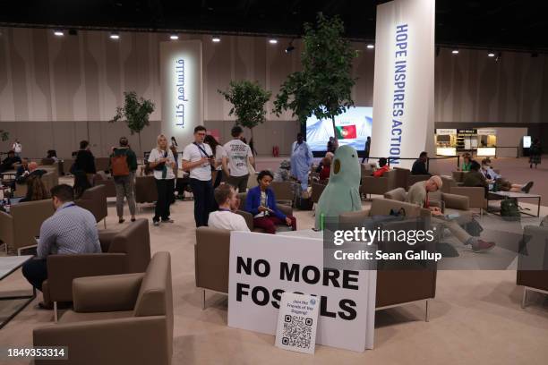 Participants, including activists with a sign that reads: "No More Fossils," wait for a result on day twelve at the UNFCCC COP28 Climate Conference...