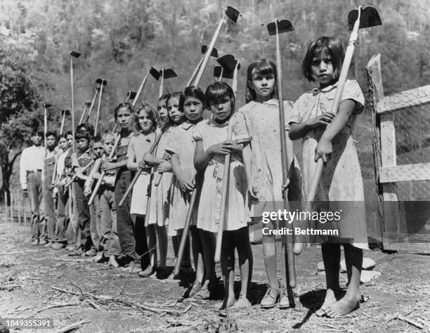 Cherokee children stand with hoes after planting victory garden at a boarding school, US, circa 1943.