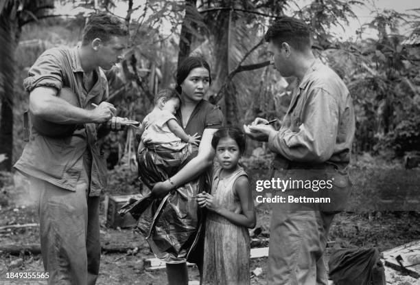 War correspondents Robert 'Pepper' Martin , of Time Magazine, and Howard Handleman, of International News Service, with a Chamorro woman and two...