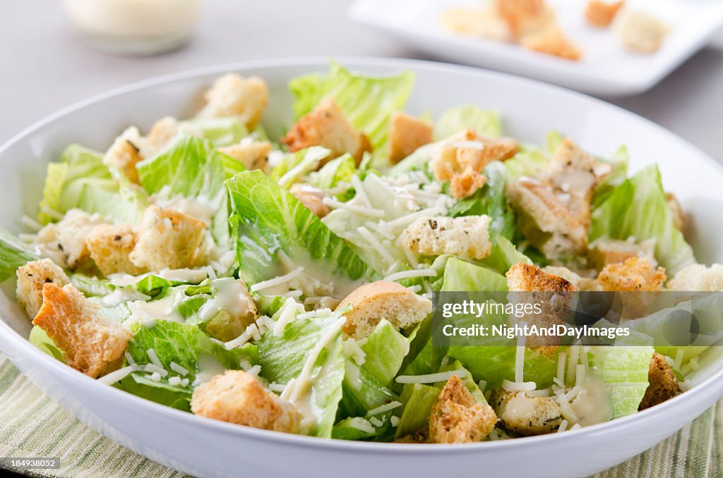 A bowl of Caesar Salad with croutons and cheese on table