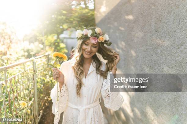 schöne braut im kleid mit blumenkrone und gelber blume in der hand im hinterhof an sonnigen tagen - blumenkrone stock-fotos und bilder