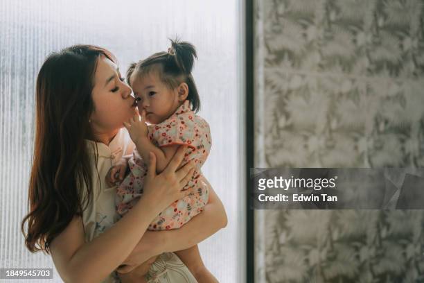 chinese new year chinese mother kissing daughter bonding time at home in morning - the cheongsam stock pictures, royalty-free photos & images