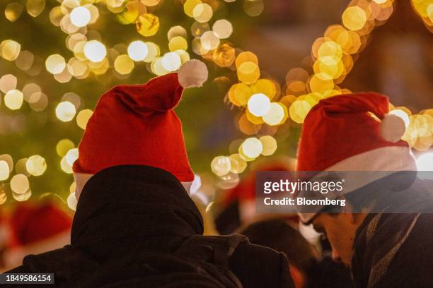 Visitors wearing Santa hats at a Christmas market, in Berlin, Germany, on Thursday, Dec 14, 2023. Sluggish exports are dragging down industry,...