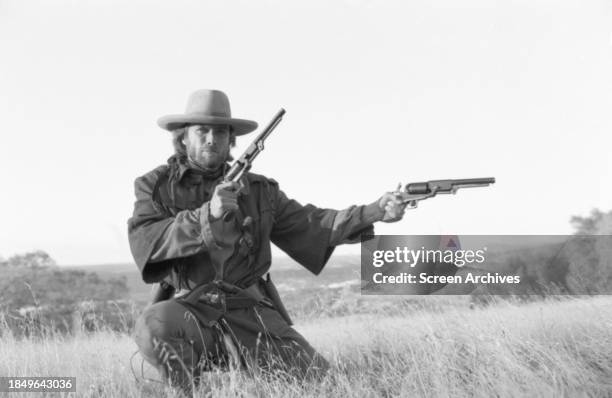 Clint Eastwood poses for publicity portrait firing two guns from the 1976 western 'The Outlaw Josey Wales'.