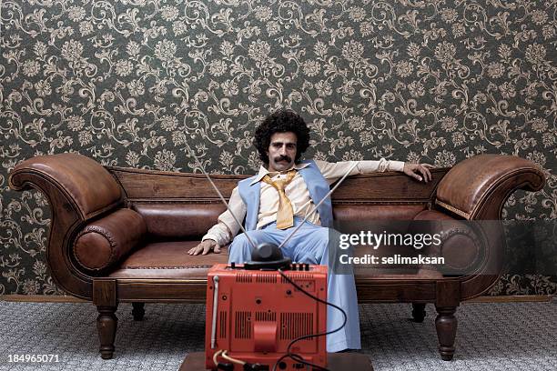hombre en 1970 estilo, sentado en el sofá mientras ve la televisión - film 2012 fotografías e imágenes de stock