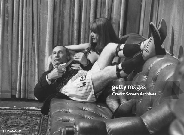 Mel Brooks plays ukelele as he lays on couch with Robyn Hilton in a scene from his 1974 film 'Blazing saddles'.