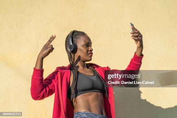 african woman standing outdoors and taking selfie. - fashion pretty woman listening music in headphones with smartphone colorful stockfoto's en -beelden