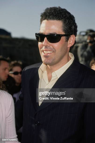 American comedian, actor and radio presenter Adam Carolla, wearing sunglasses, attends the 1999 MTV Movie Awards, held at the Barker Hangar, at Santa...