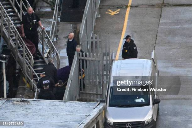 Police officers stand by the steps of the Bibby Stockholm Barge as a body is brought out on a gurney and taken to the funeral van for the coroner on...