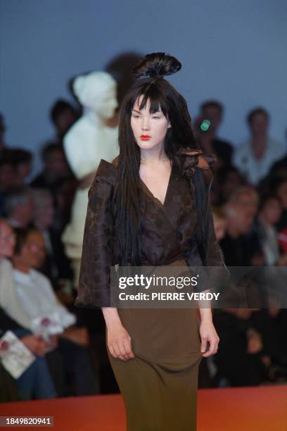 Model, with a geisha hairstyle, presents a white kimono under a sleeveless denim jacket on a long white skirt by Jean-Paul Gaultier for his...