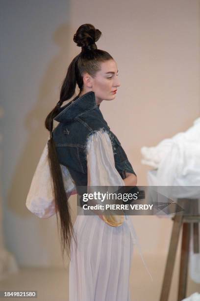 Model, with a geisha hairstyle, presents a white kimono under a sleeveless denim jacket on a long white skirt by Jean-Paul Gaultier for his...