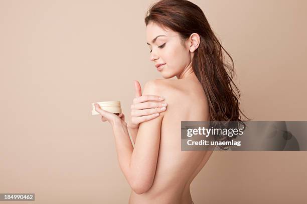 a woman rubbing lotion on her naked arm - woman face close up stock pictures, royalty-free photos & images