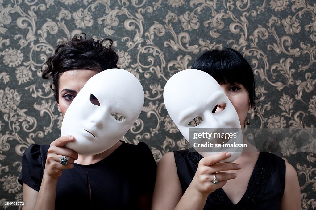 Two women peeking behind mask on wallpaper background