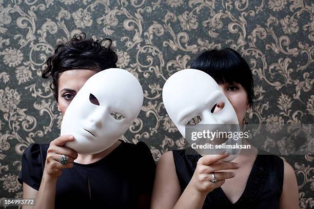 two women peeking behind mask on wallpaper background - acting performance stock pictures, royalty-free photos & images