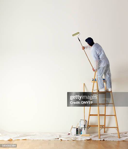 house painter standing on ladder una gran pared de pintura - pared casa fotografías e imágenes de stock