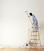 House painter standing on ladder painting a large wall