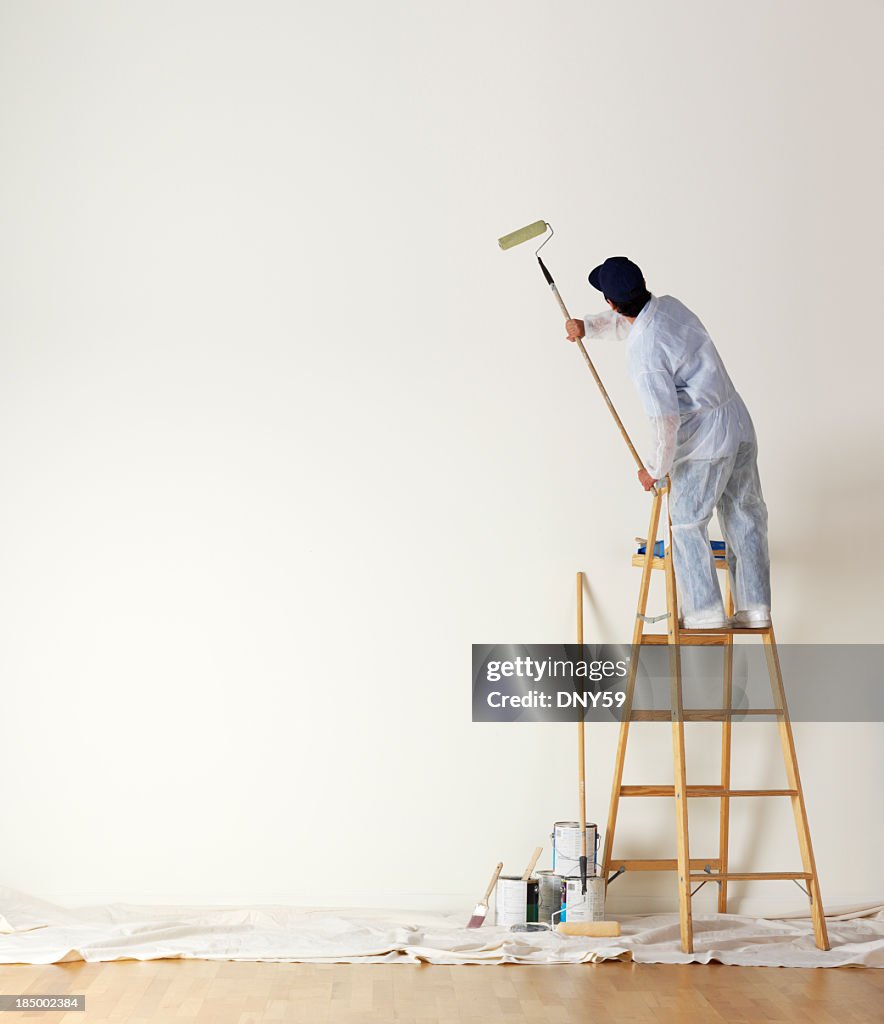 House painter standing on ladder painting a large wall
