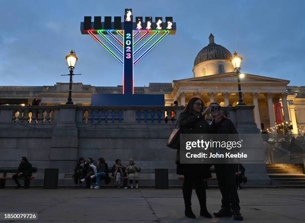 People take a selfie against a giant menorah, lit up for Hanukkah, the Jewish festival of lights in Trafalgar Square on December 11, 2023 in London,...