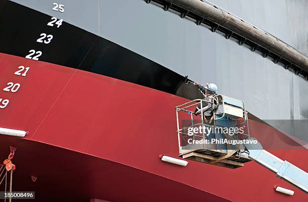 man painting ship's hull with roller - ship building stockfoto's en -beelden