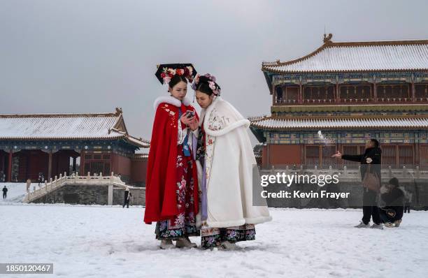 Women wear traditional Hanfu clothing as they look at a mobile phone while visiting the Forbidden City a day after the first snowfall of the winter...