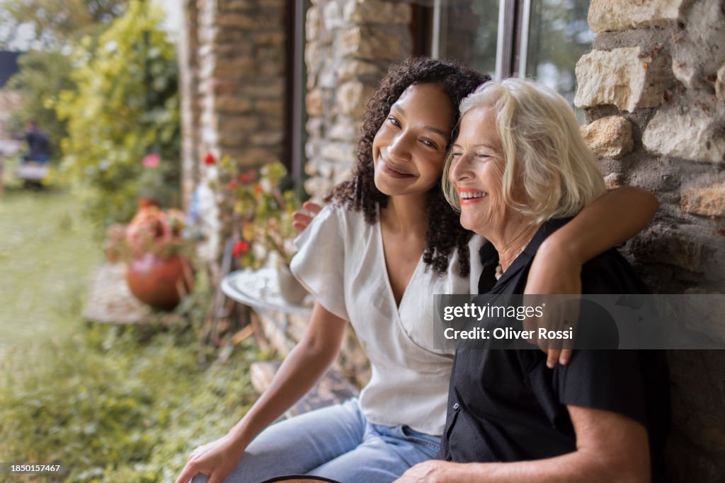 Happy granddaughter and grandmother sitting at stone house