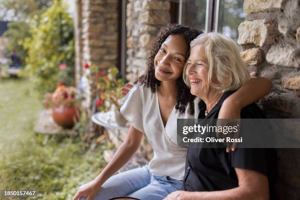 happy granddaughter and grandmother sitting at stone house - diferença entre gerações - fotografias e filmes do acervo