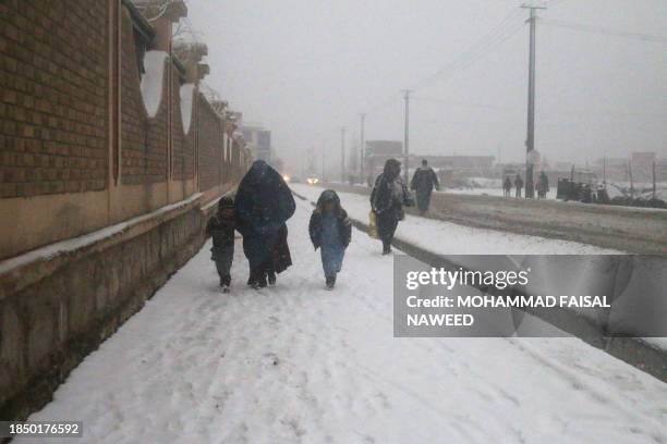 An Afghan woman walks with children along the roadside during season's first snowfall in Ghazni on December 15, 2023.