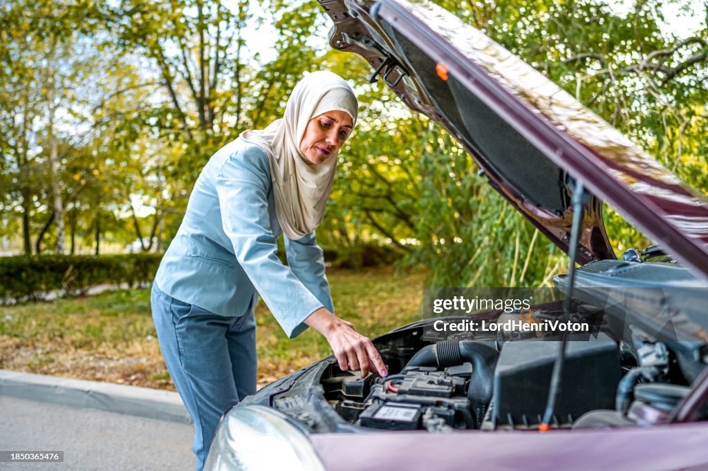 Femme musulmane mature regardant le moteur d’une voiture cassée
