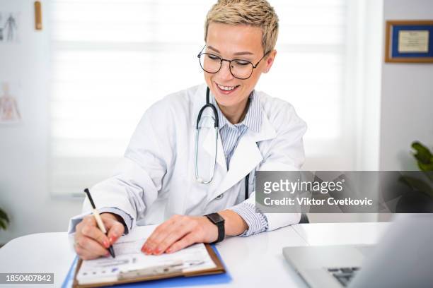 female doctor writing on a patient medical chart at the doctors office - wijding stockfoto's en -beelden