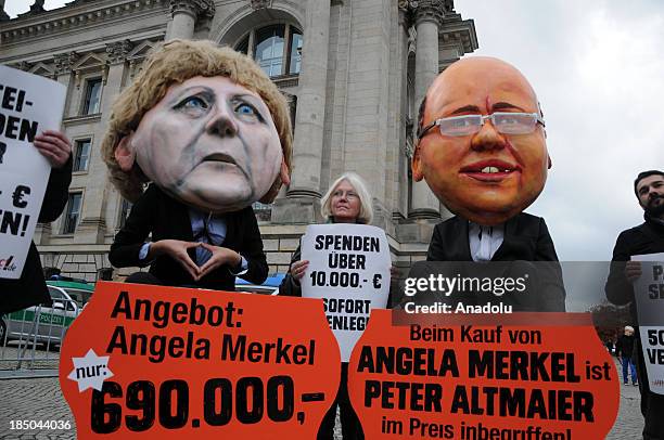 Protestors wearing masks of German Chancellor Angela Merkel and German Environment Minister Peter Altmaier sit in shopping trolleys during a protest...