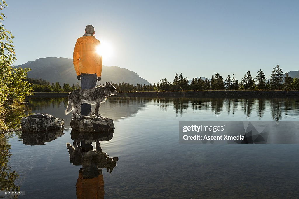 Man wtahces sunrise over mountains, with dog