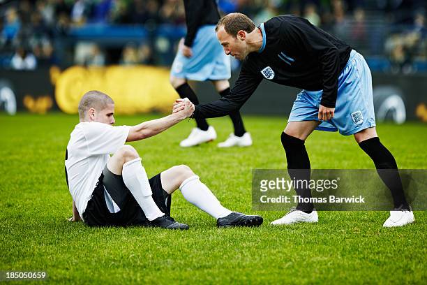 soccer player helping opposing player up - honra fotografías e imágenes de stock