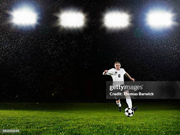 soccer player dribbling ball on field in rain - reflector objeto fabricado fotografías e imágenes de stock