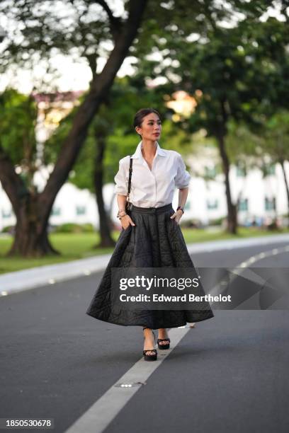 Heart Evangelista wears earrings, a white shirt, a black leather Dior bag, a Dior black quilted midi skirt, black shoes with high heels, during a...