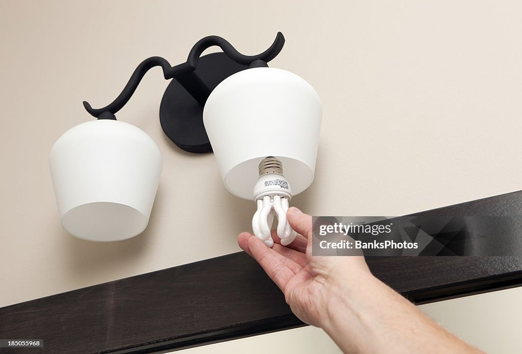 Hand installing Compact Fluorescent Light Bulb into Fixture