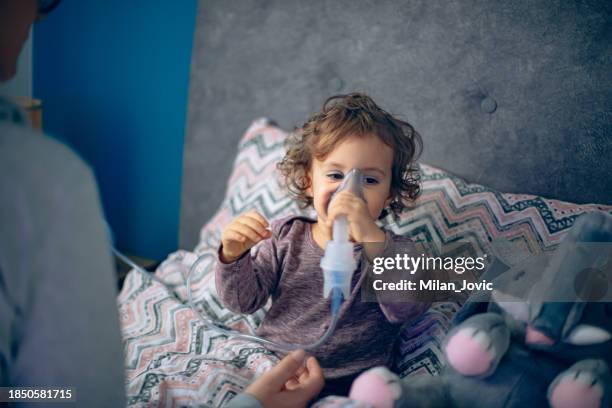 mutter hilft ihrer kleinen tochter beim einatmen mit einem vernebler - mukoviszidose stock-fotos und bilder