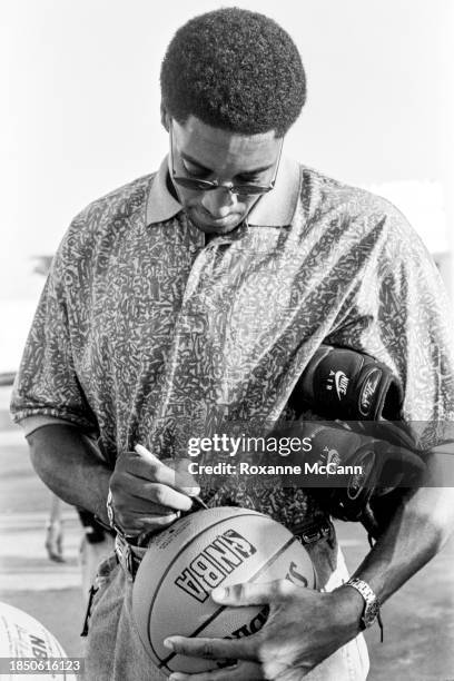 Scottie Pippen of the Chicago Bulls autographs a Spaulding NBA basketball wearing sunglasses, a collared print shirt, a bracelet, watch, and jeans...