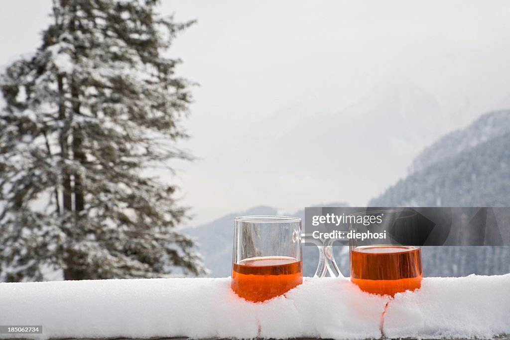 Two glasses of drink sit on a snow covered ledge
