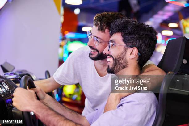 gay couple playing and having fun with a driving simulator in an amusement arcade. - arcade stockfoto's en -beelden
