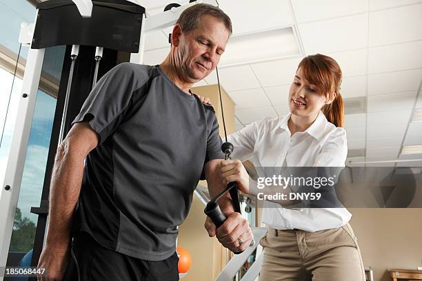 physical therapist instructing man on proper use of exercise equipment - exercise machine stock pictures, royalty-free photos & images
