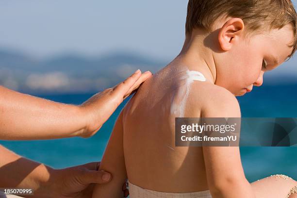woman applying sunscreen on a child's back at the beach - baby suncream stockfoto's en -beelden