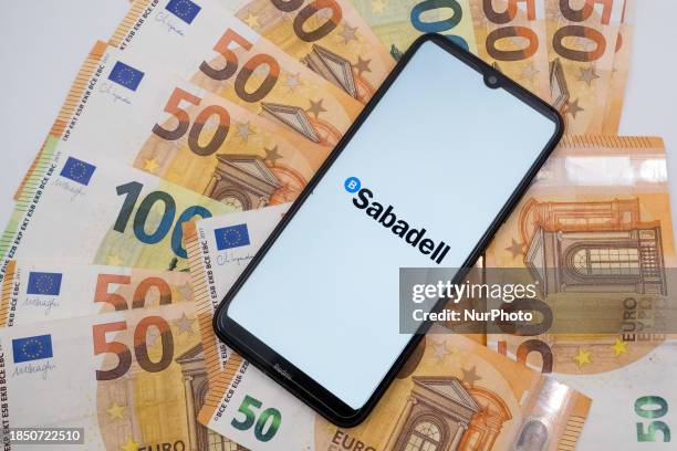 The Sabadell logo is displayed on a smartphone screen placed on 50 and 100 Euro bills in Athens, Greece, on December 15, 2023.