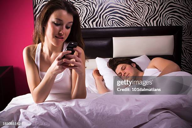 woman texting while in bed with sleeping man - unfaithful husband stock pictures, royalty-free photos & images