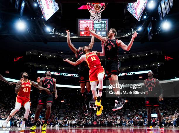 Trae Young of the Atlanta Hawks goes to the basket against Jakob Poeltl and Scottie Barnes of the Toronto Raptors during the second half of their...